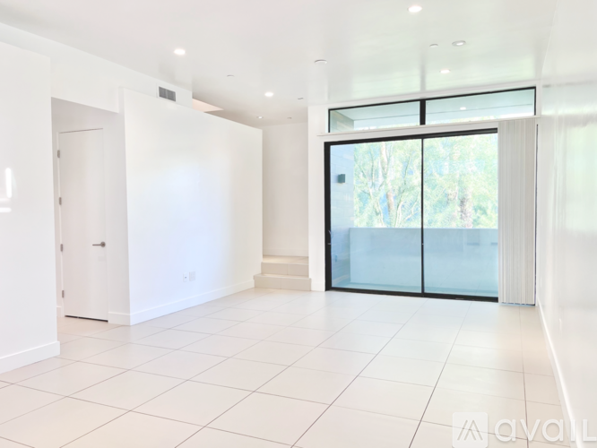 A spacious, white-walled room with a tiled floor and a large glass door leading outside.