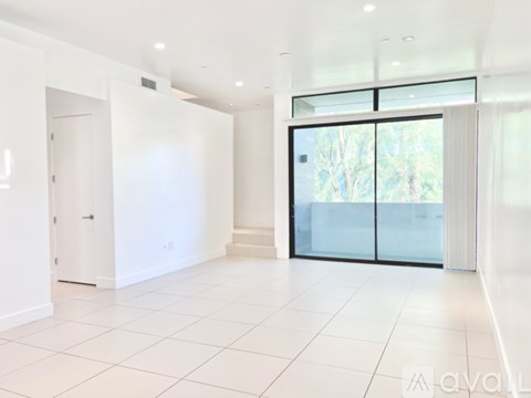 A spacious, white-walled room with a tiled floor and a large glass door leading outside.