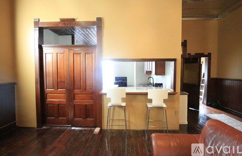 A room with a brown door and a bar area with white chairs.