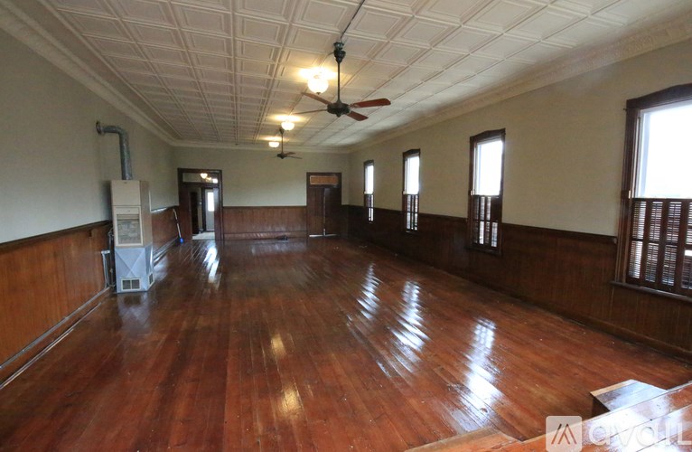 A large empty room with wooden floors and a ceiling fan.