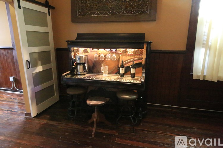 A bar with a black counter and stools is in a room with wooden floors and a wooden cabinet.
