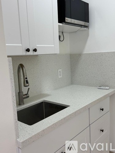 A kitchen with white cabinets and a black microwave.