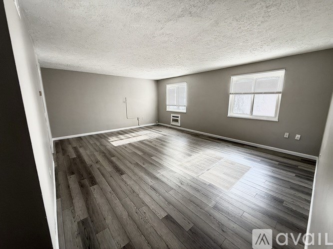 A room with wooden flooring and two windows.