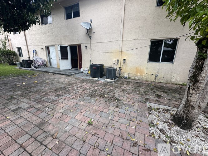 A brick patio is in front of a tan building with a satellite dish on the roof.