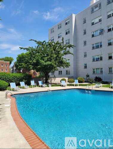 A pool in front of a white building with chairs around it.
