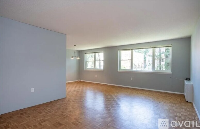 A spacious room with wooden flooring and two windows.