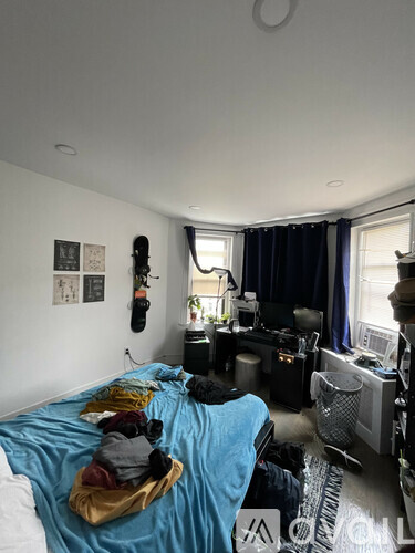 A bedroom with a bed covered in clothes and a computer desk with a monitor and keyboard.