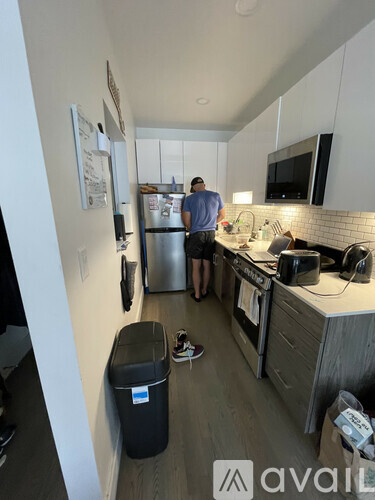 A man is standing in a kitchen with a refrigerator, microwave, and oven.