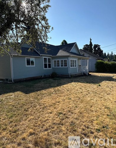 A house with a grey roof and white walls is surrounded by a grassy field.