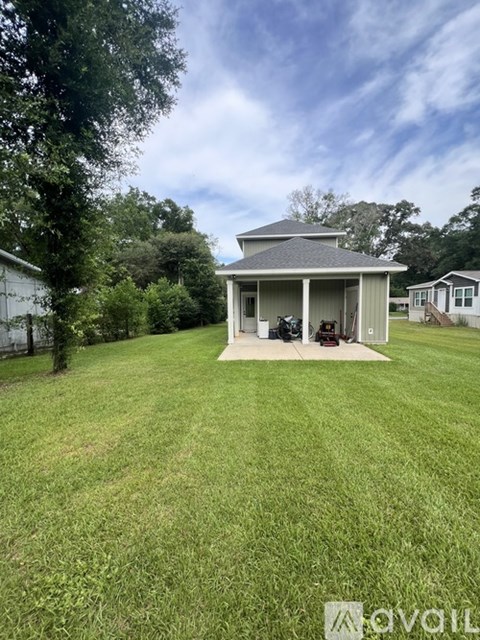 A small house with a covered patio is surrounded by a grassy yard.