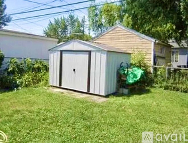 A shed with a grey door is situated in a grassy area.