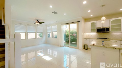 A spacious kitchen and living room with white cabinets and a marble countertop.