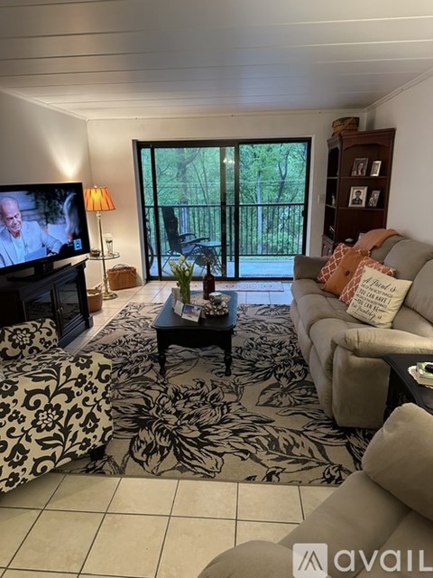 A living room with a television on, a sofa, a coffee table, and a view of a balcony through the glass doors.