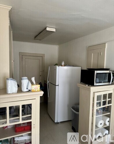 A kitchen with a white fridge, a microwave on top of a cabinet, and a cabinet with glass doors.