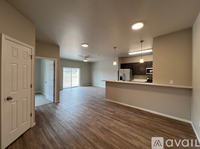 A spacious room with wooden flooring and a kitchen area in the background.