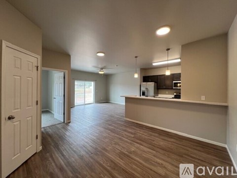 A spacious room with wooden flooring and a kitchen area in the background.