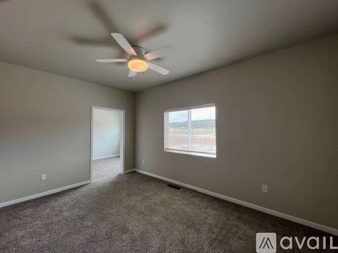 A room with a ceiling fan and a window with a view of a fence.