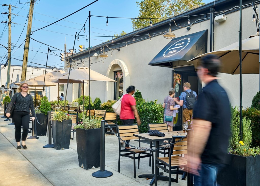 A busy outdoor cafe scene with people walking and sitting at tables.