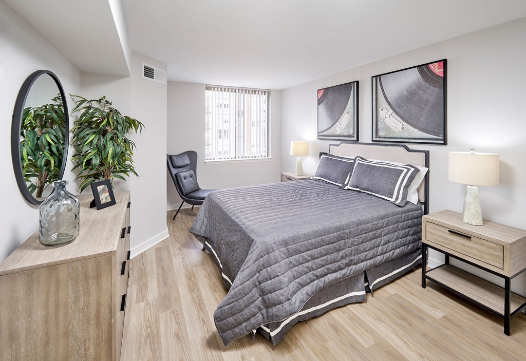 A bedroom with a bed, nightstand, and a plant.