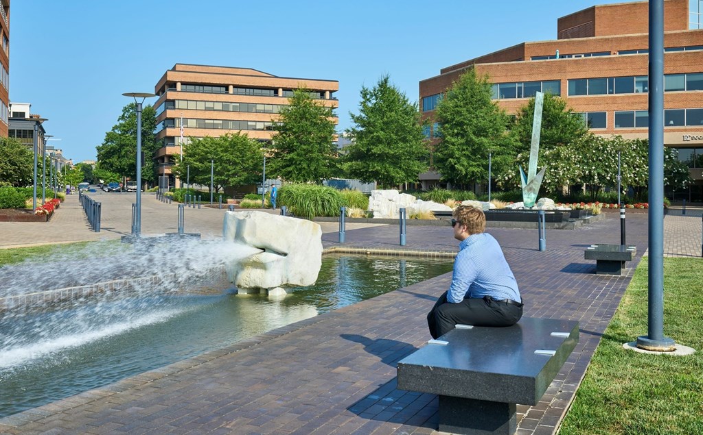 A man sits on a bench by a water feature.