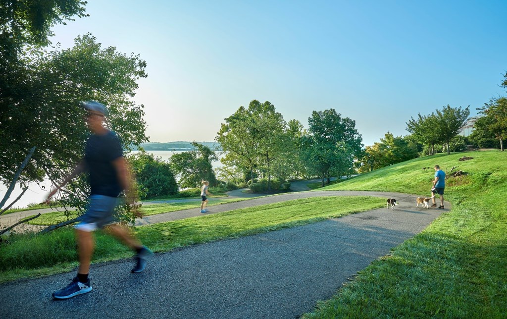 A man is jogging on a paved path in a park.