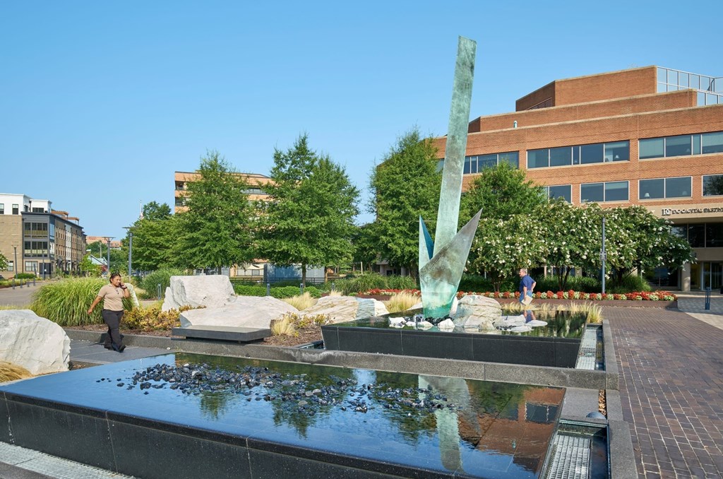 A person walks past a water feature in a courtyard with a large green sculpture.