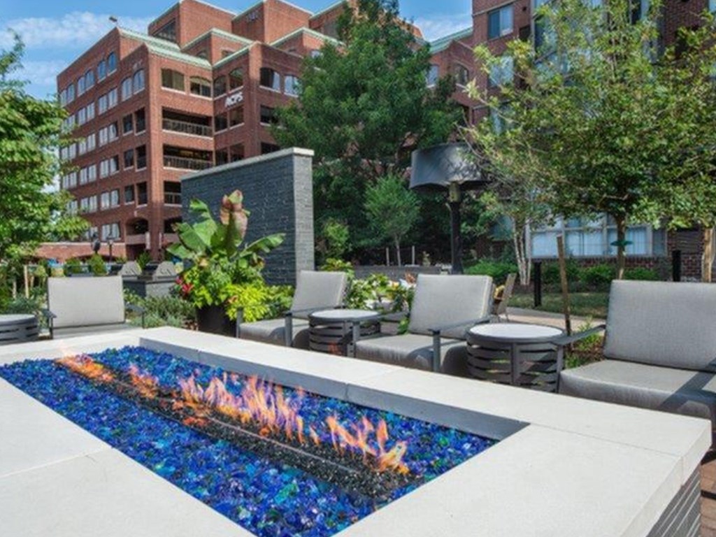 A modern fountain with blue and orange water is in the foreground of a city park.