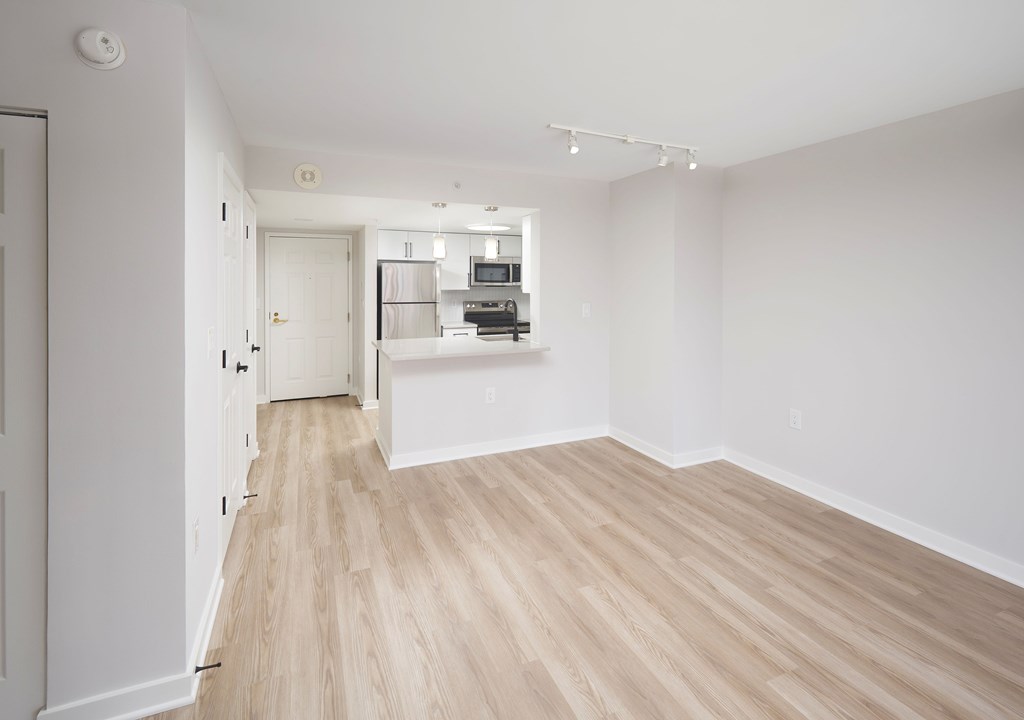 A long, empty room with light wood flooring and white walls.