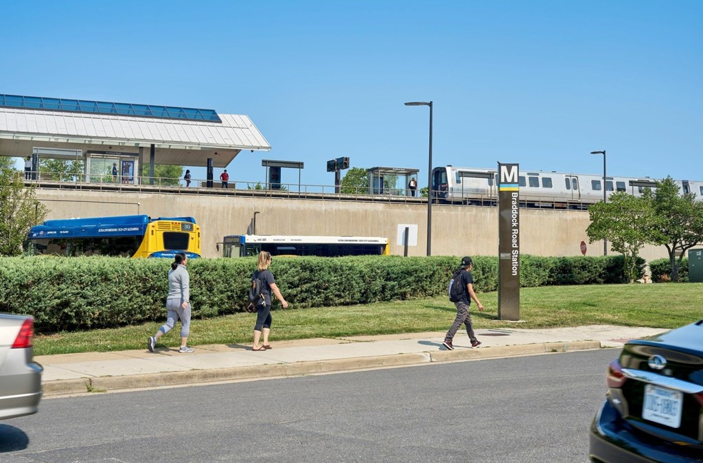 A train station with a train on the tracks and people walking on the sidewalk.