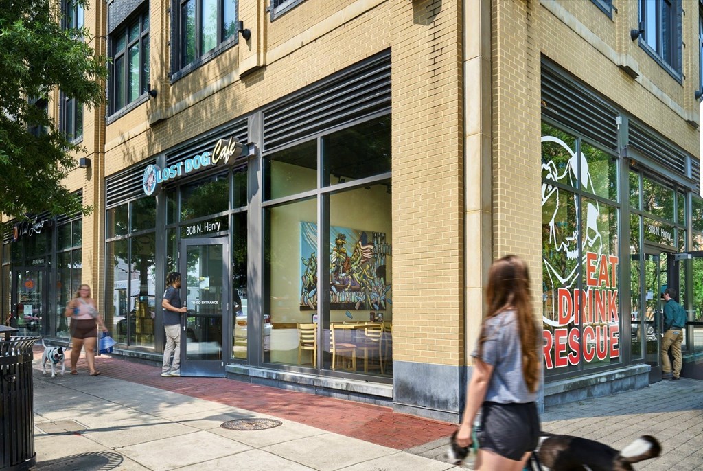 A woman walks her dog past a restaurant with a sign that says "Eat Dinner Rescue".