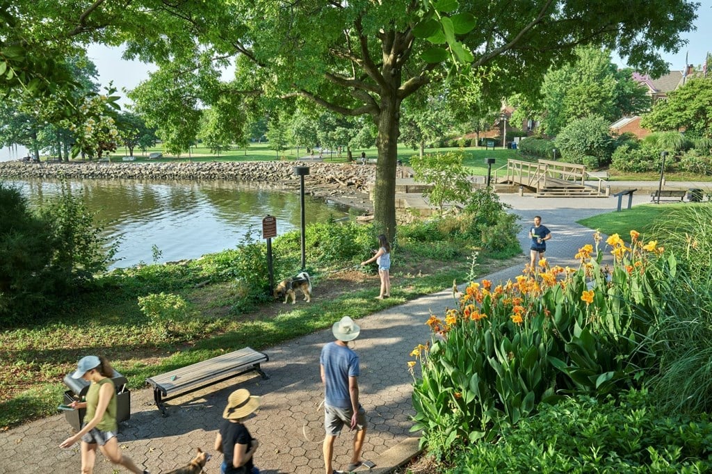 A family is walking along a path in a park with a pond and flowers.