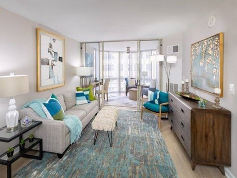 A living room with a grey couch, a blue rug, and a painting on the wall.