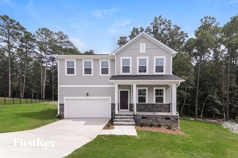 A two-story house with a garage is surrounded by a grassy lawn and trees.