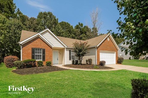 A house with a brown brick exterior and a white garage door is surrounded by a well-manicured lawn.