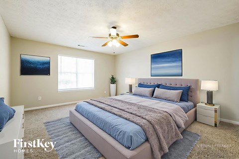A bedroom with a large bed, a ceiling fan, and two pictures on the wall.