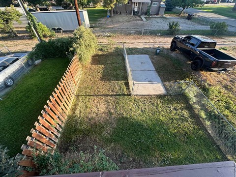 A black truck is parked on a grassy area next to a wooden fence.