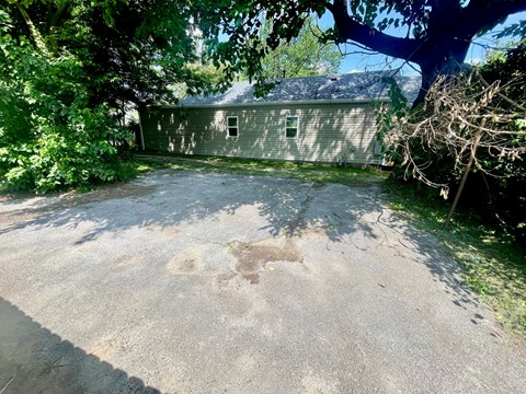 A concrete driveway leads to a house with a grey siding and a white door.