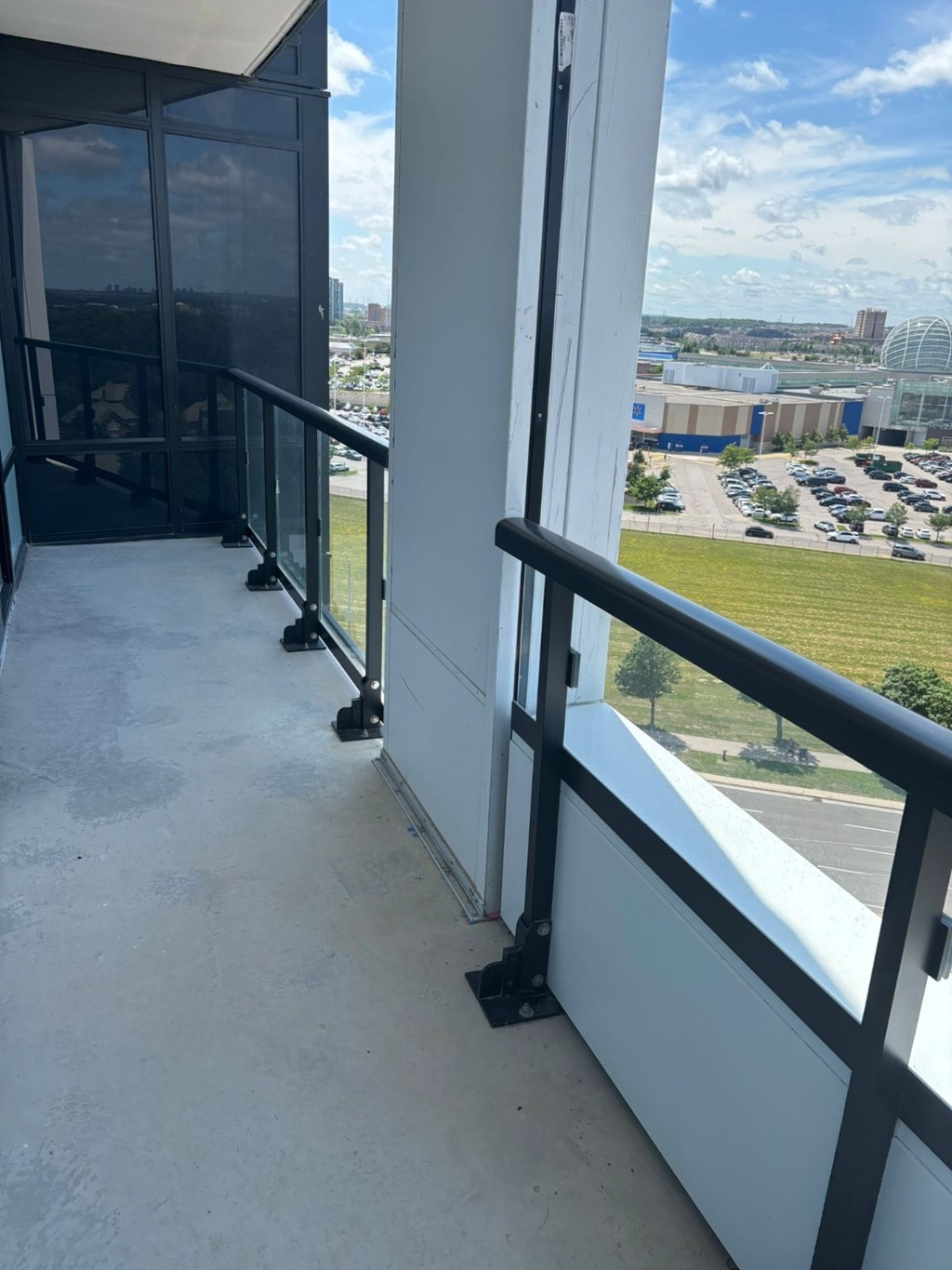 A balcony with a metal railing and glass doors overlooking a parking lot.