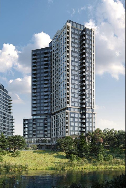 A modern high-rise building with balconies is surrounded by greenery and other buildings.