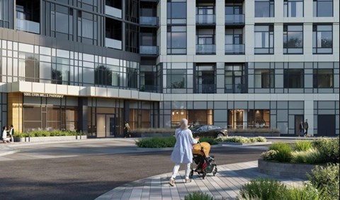 A woman in a blue coat walks with a stroller in front of a modern building.