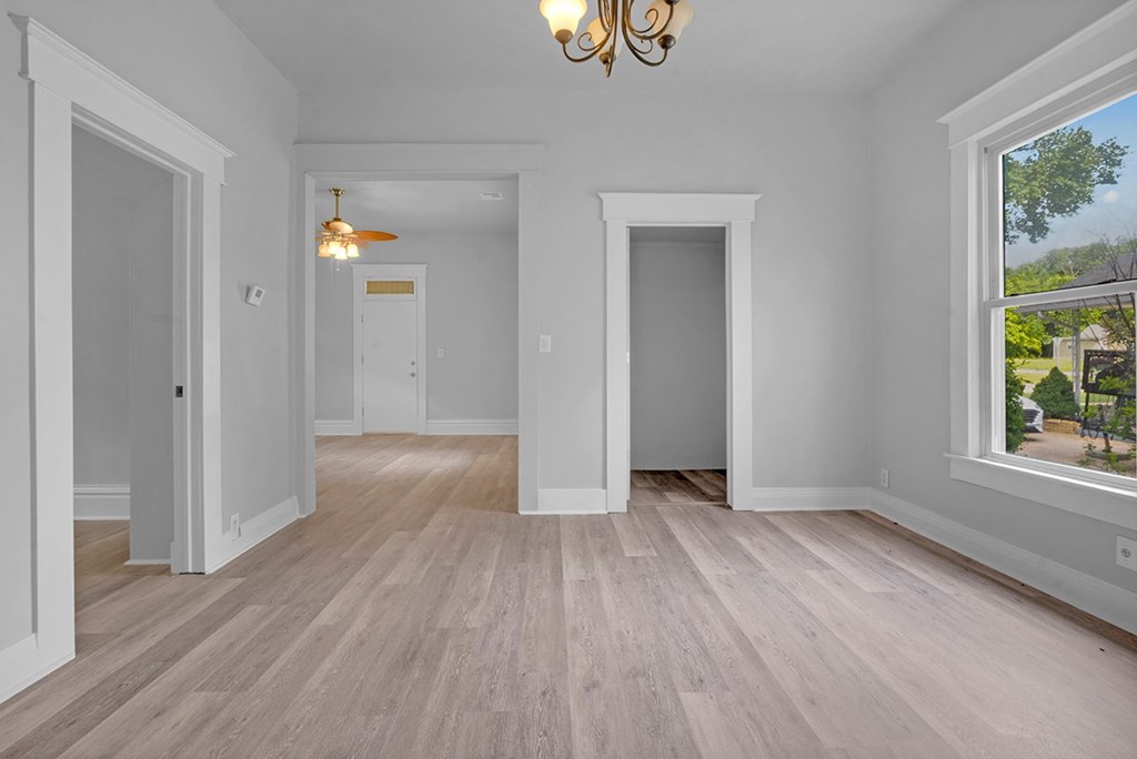 A room with white walls and wooden flooring with a chandelier hanging from the ceiling.