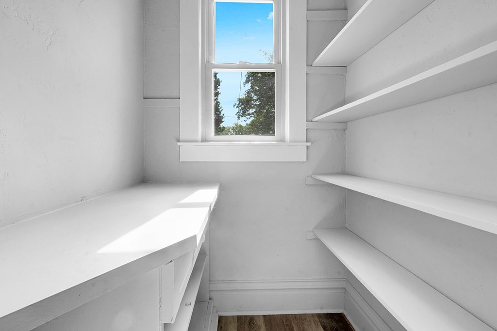 A white pantry with a window seat and a view of a tree.