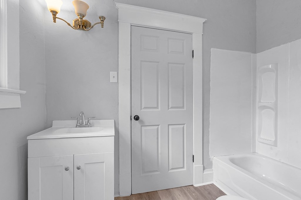 A white bathroom with a white tub, sink, and door.