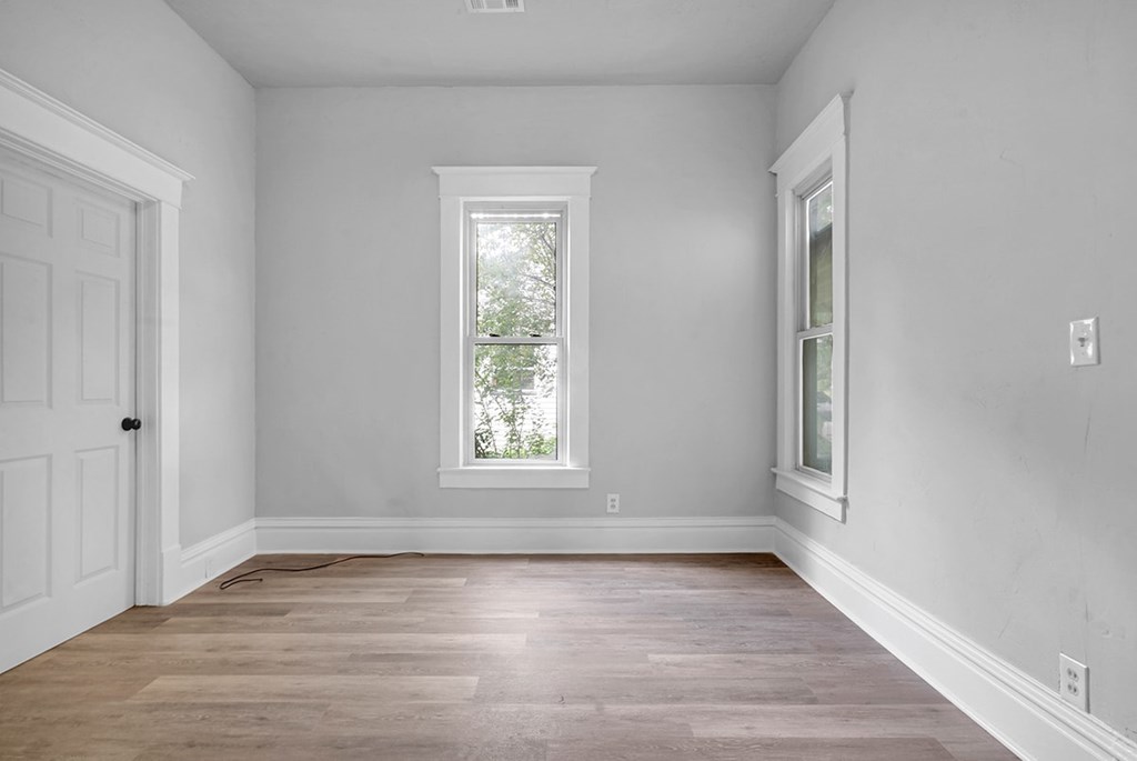 A room with a white door, window, and wooden floor.