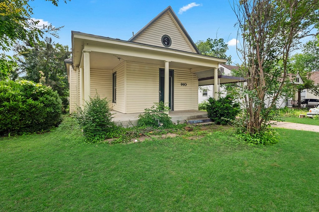 A small house with a front porch and a tree in front of it.