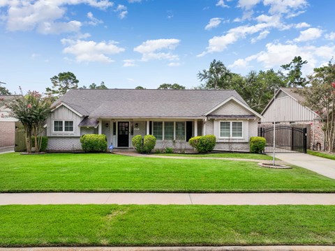 A house with a grey roof and white walls is surrounded by a green lawn.