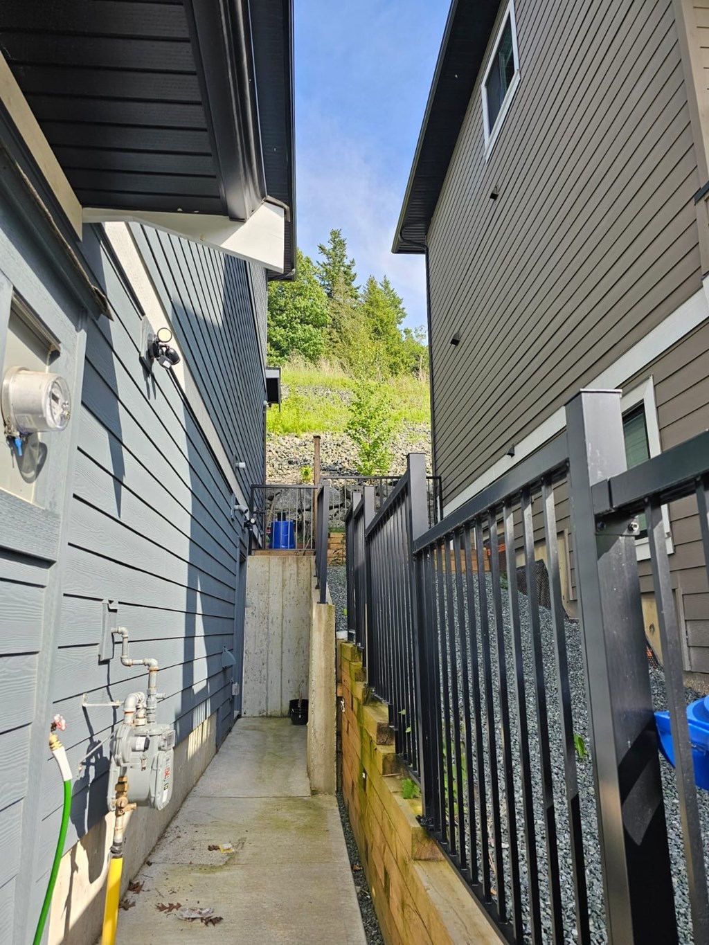 A narrow alley between two houses with a metal fence on the right side.