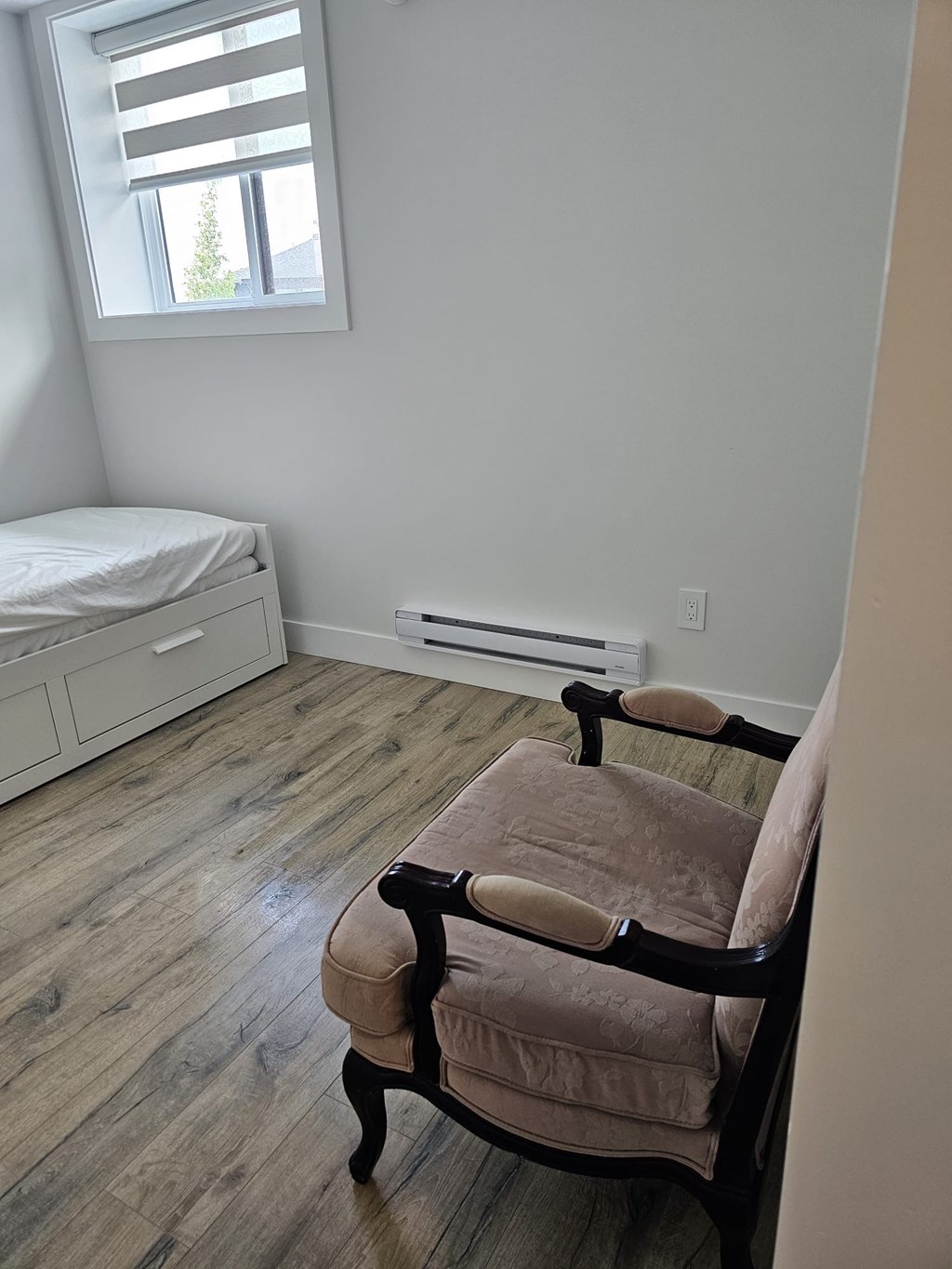 A chair with a brown cushion is in the corner of a room with a window.