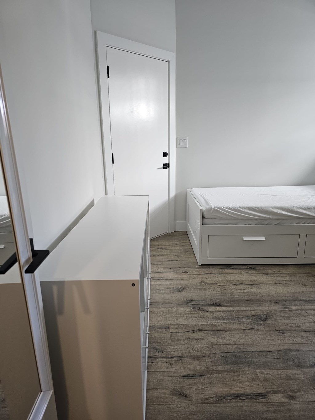 A white bedroom with a bed, dresser, and mirror.