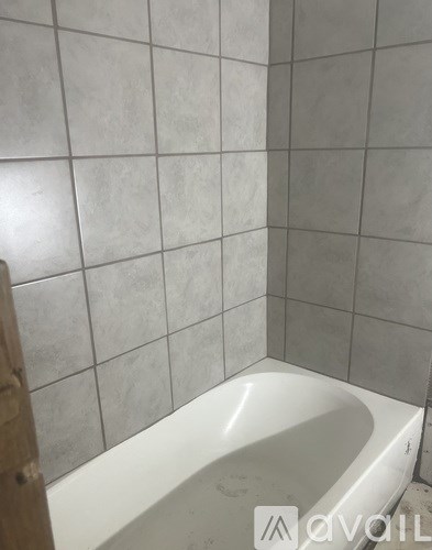 A white bathtub in a bathroom with grey tiled walls.